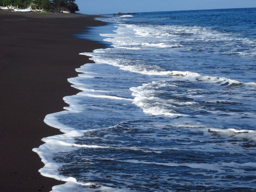 Black volcanic sand beach in Bali with foam-line waves