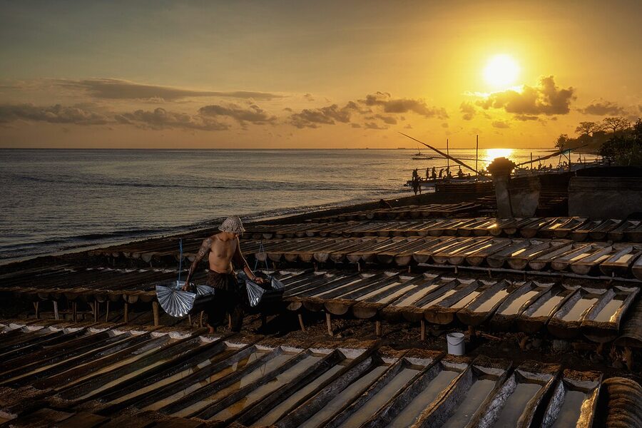 Traditional Balinese salt farmer working wooden evaporation troughs at sunset
