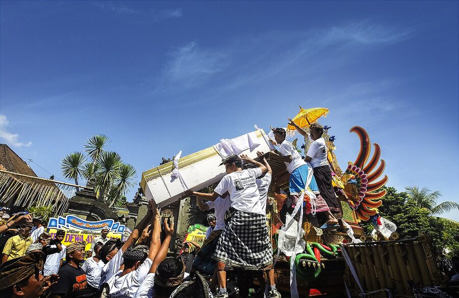 A wadah cremation tower carried in procession during a Balinese ngaben ceremony, with mourners in white and black ceremonial dress