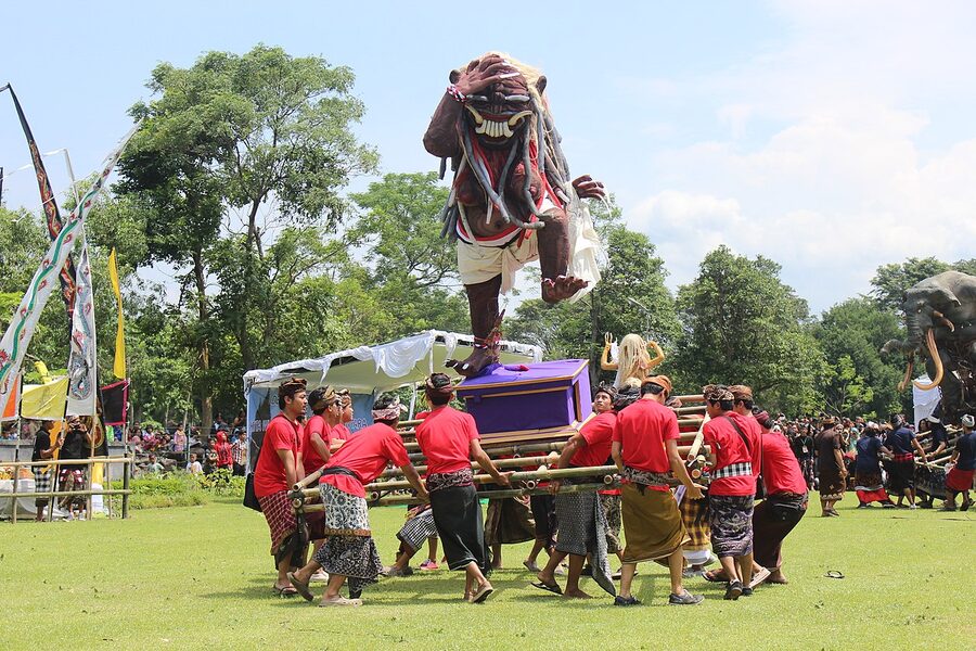 A large papier-mache ogoh-ogoh demon effigy carried on a bamboo platform by men in red shirts during a Bali parade