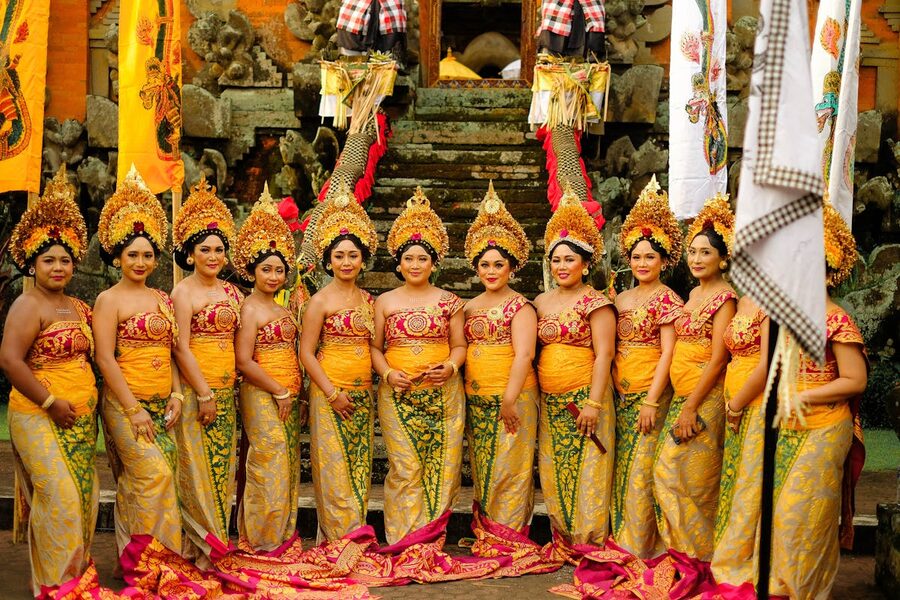 A row of Balinese women dressed in matching gold and red traditional kebaya at a temple in Bali
