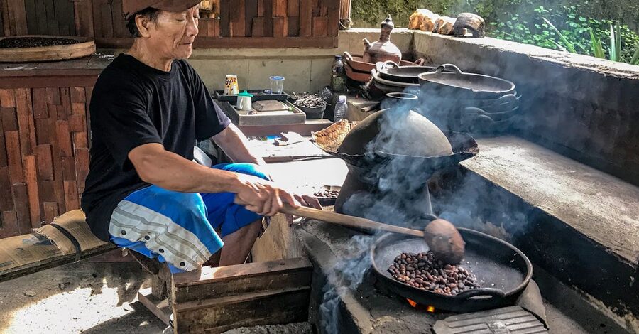 A Balinese man hand-roasting coffee beans in a traditional kitchen