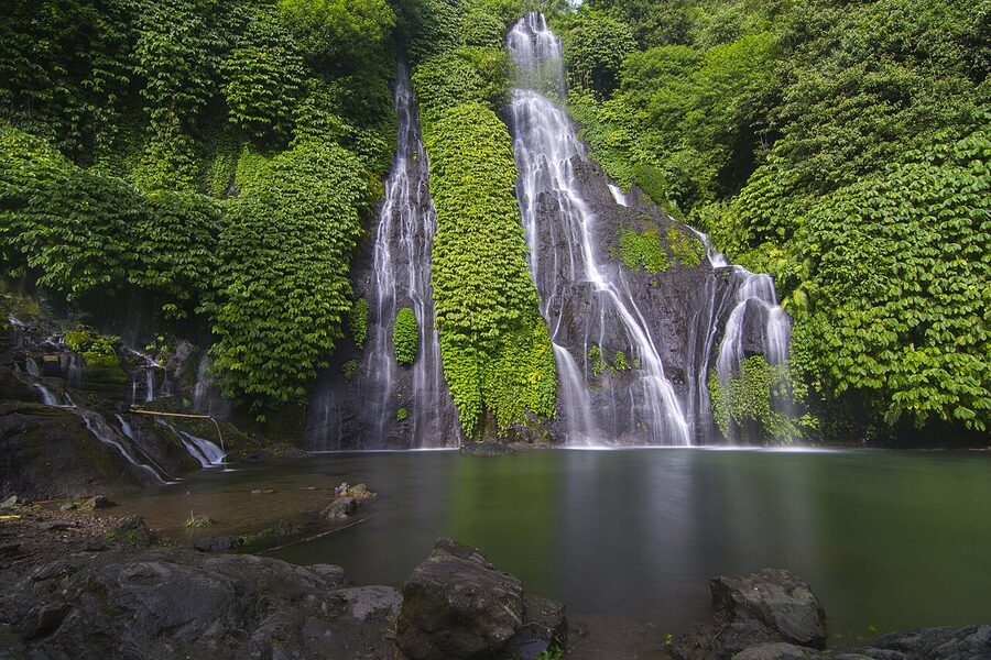 Banyumala Twin Waterfall, two parallel cascades over a moss-covered cliff into a green pool