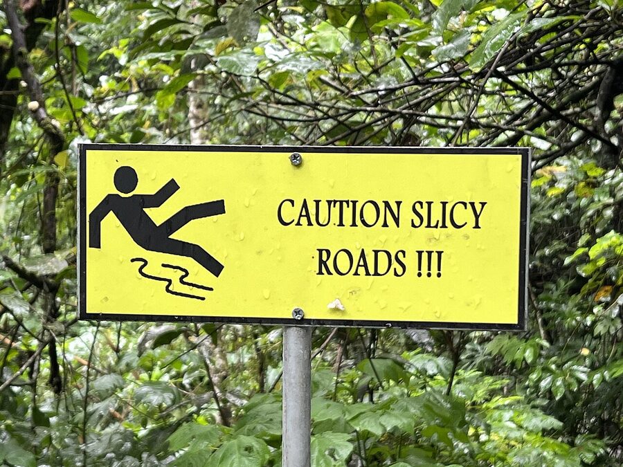 Caution slippery roads sign on a wet jungle trail near Munduk waterfalls