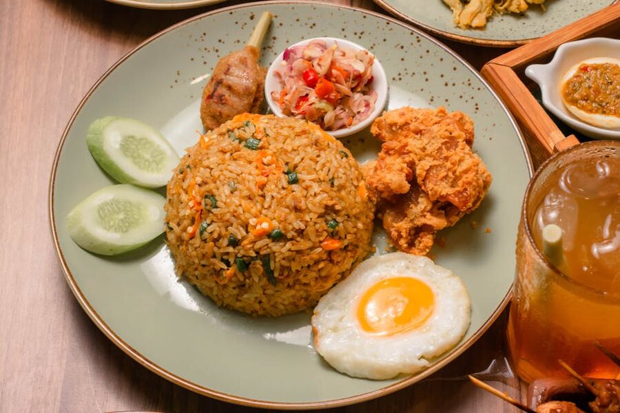Plate of nasi goreng with a fried egg, sate skewers, and iced tea at a Munduk warung