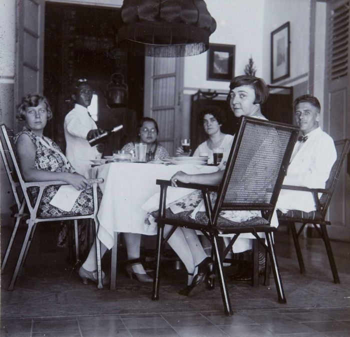 Black and white archival photo of a Dutch family seated at a table in colonial Java being served by an Indonesian waiter