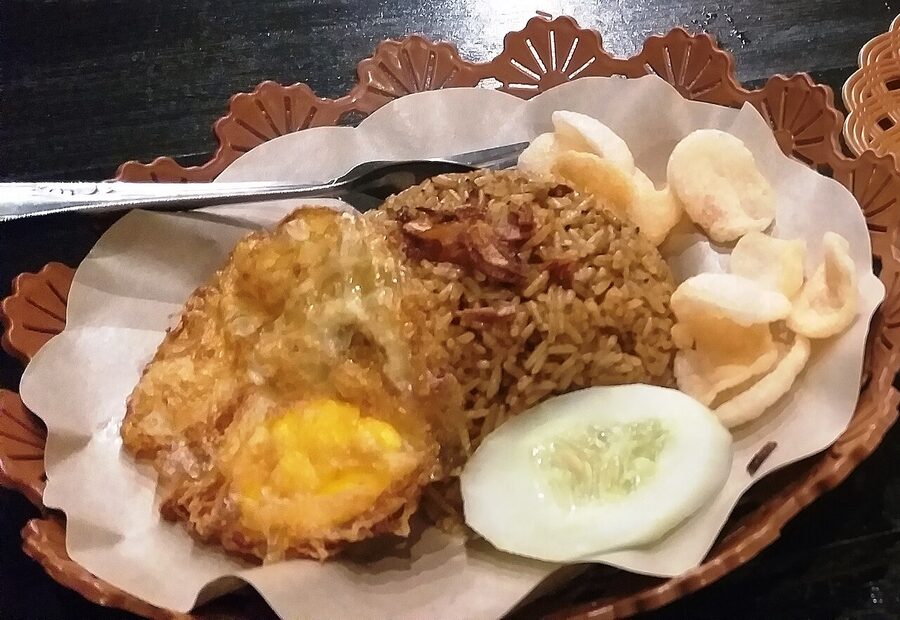 A plate of nasi goreng kampung village style with rice, kerupuk, fried egg and sliced cucumber on patterned paper