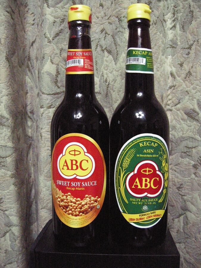 Two bottles of ABC brand Indonesian soy sauce, the red label sweet kecap manis on the left and the green label salty kecap asin on the right