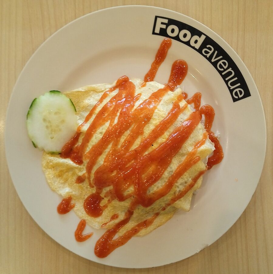 Nasi goreng pattaya, a parcel of fried rice wrapped in a thin omelette and drizzled with chilli sauce, served on a white plate