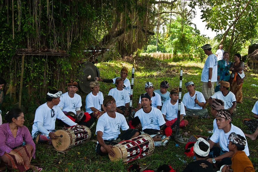 Gamelan beleganjur musicians in white seated at ngaben procession Bali
