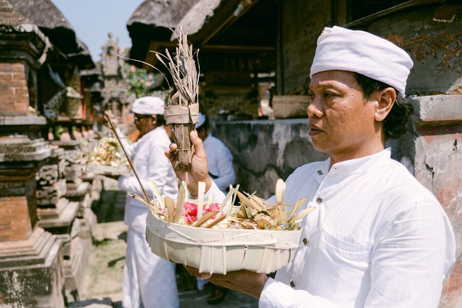 Balinese pemangku priest in white holding traditional offerings during a ceremony