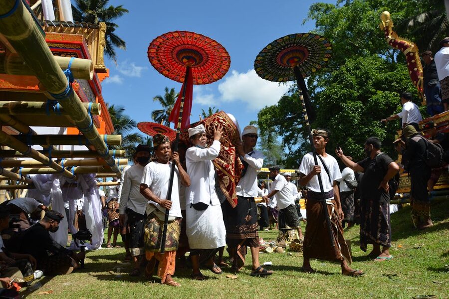 Balinese ngaben procession with ceremonial red umbrellas and bearers in white