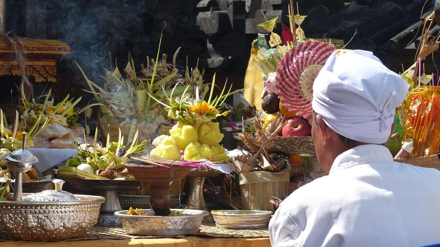 Balinese temple altar with fruit offerings smoke and priest in white during ceremony