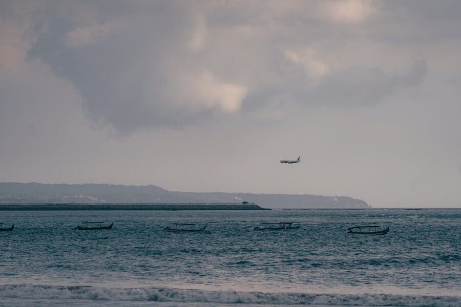 Airplane descending over Kuta Bali coastline with traditional jukung boats below