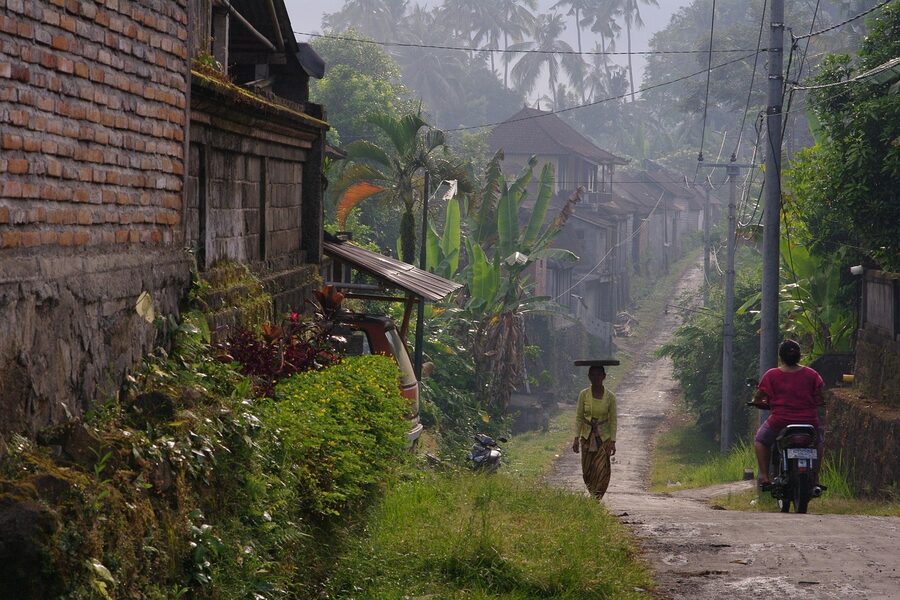 Bali back lane at dusk with a woman walking and moped passing