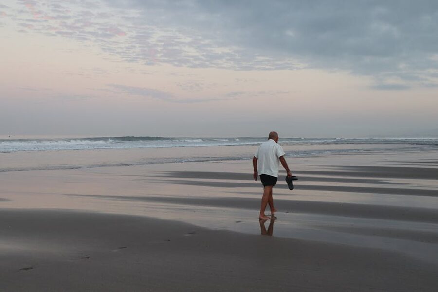 Older man walking on a Bali beach at sunrise with sandals in hand