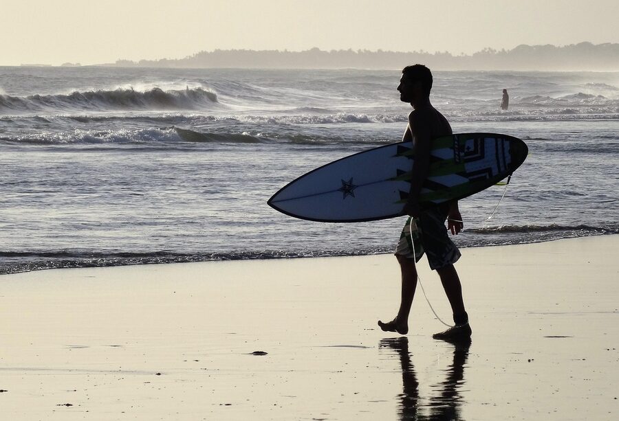 Bali surfer carrying his board at golden hour silhouetted against the waves