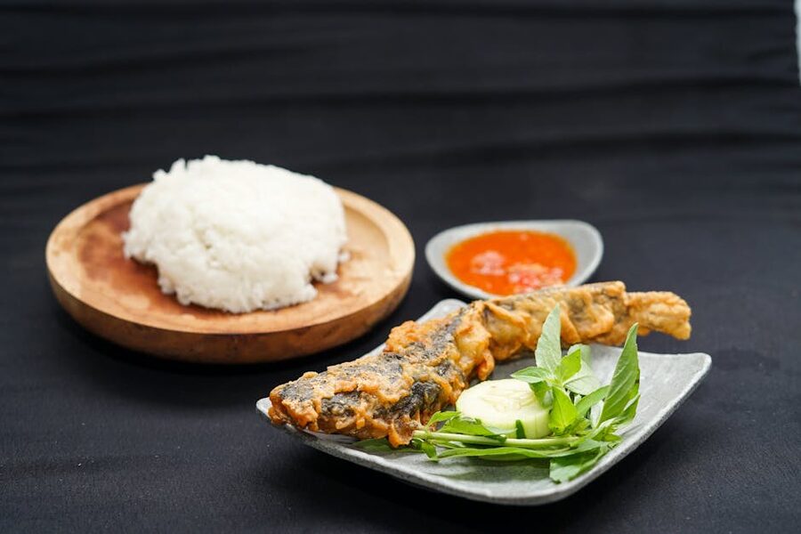Crispy whole fried fish served with rice and red sambal on a white plate