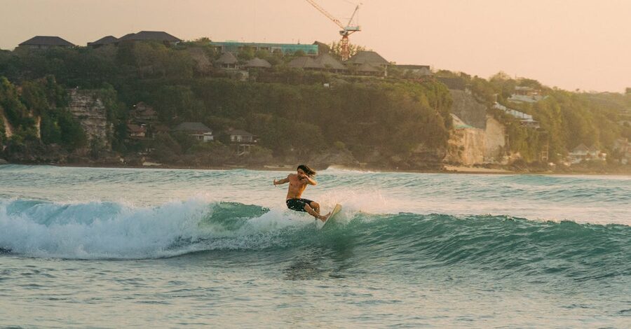 Surfer riding a wave at sunset below the limestone cliffs of the Bukit Bali, near Bingin