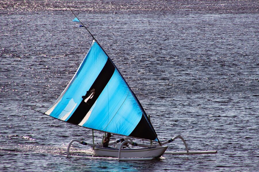 A Bali fisherman returning home with a bright blue triangular sail