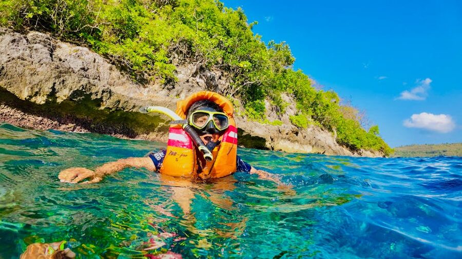 Snorkeler in clear blue water near a rocky shore in Bali