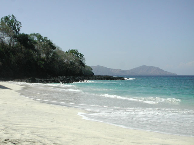 A white sand beach at Padangbai with rocks and a forested headland and Lombok in the distance